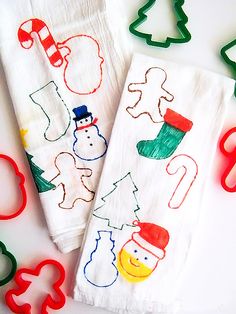 two kitchen towels decorated with christmas images and cookie cutters next to each other on a table