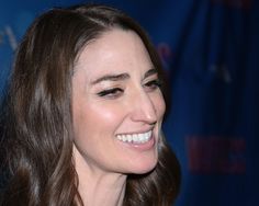 a close up of a person with long hair and wearing a black dress smiling at the camera