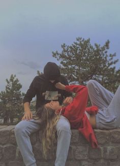 two people sitting on top of a stone wall