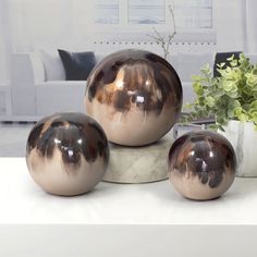 three metallic vases sitting on top of a table next to a potted plant