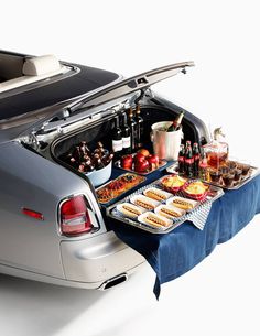 an open trunk with food and drinks in it on a table next to a car