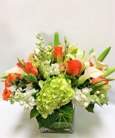 an arrangement of flowers in a square vase on a table top with white and green foliage