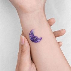 a woman's hand with a purple tattoo on her wrist and the moon in the background