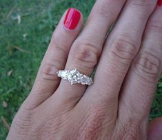 a woman's hand with a three stone ring on top of her finger and red nail polish