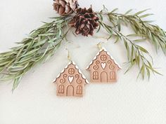 two wooden houses with hearts are hanging from pine needles and decorated with greenery, next to a pine cone