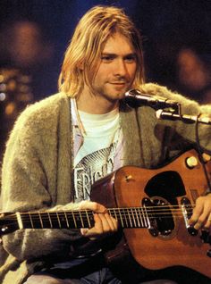 a man sitting in front of a microphone while holding a guitar