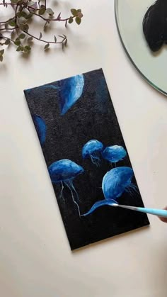 someone is painting some blue flowers on a piece of black paper with a paintbrush