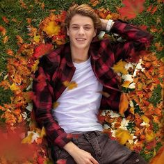 a young man laying on the ground surrounded by autumn leaves and fallen leaves, with his hands behind his head