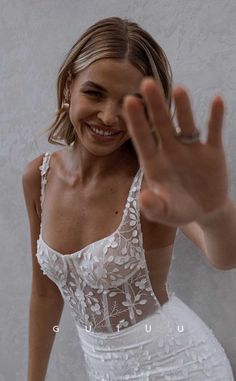 a woman in a white dress is smiling and waving her hand up to the camera