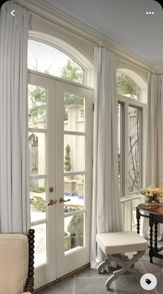 a living room filled with furniture and large windows covered in white draping next to a door