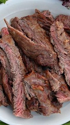 a white plate topped with sliced meat on top of a green table cloth next to a knife and fork