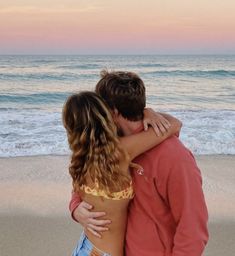 a man and woman kissing on the beach at sunset with waves crashing in to shore