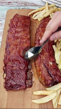 someone is cutting up some ribs and french fries on a cutting board with a spoon