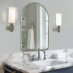 a bathroom vanity with marble counter top and two lights on the wall, along with a large oval mirror above it