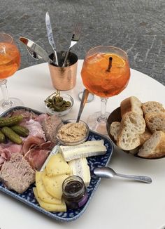 an assortment of meats and cheeses on a plate with wine glasses in the background