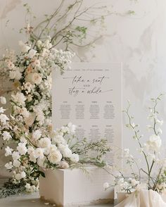 a table plan sitting on top of a white box next to flowers and greenery