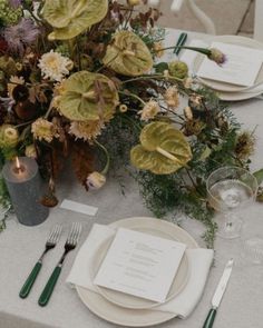 the table is set with plates, silverware and greenery for an elegant dinner