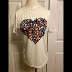 White Crew-Neck Short-Sleeved Tee With Bold Multi-Colored Heart Graphic. 65% Cotton/35% Polyester. Casual V-neck Top With Heart Print, White Heart Print T-shirt For Summer, Spring V-neck Tops With Heart Graphic, Spring V-neck Top With Heart Graphic, Multicolor Heart Graphic Crew Neck Top, Casual White Tops With Heart Graphic, Casual White Top With Heart Graphic, Multicolor Heart Print Crew Neck Top, Multicolor Short Sleeve Tops With Heart Print