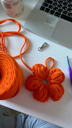 an orange piece of yarn sitting on top of a white table next to a laptop