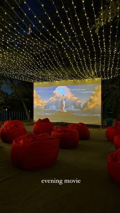 an outdoor movie screen with red bean bags on the ground