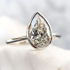 a pear shaped diamond ring sitting on top of a white cloth