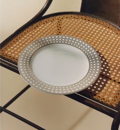 an empty white plate sitting on top of a wooden chair next to a wicker seat