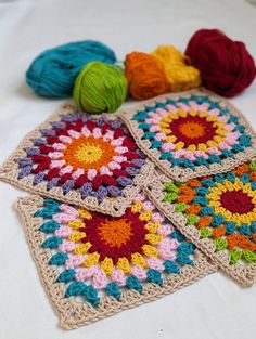 four crocheted squares with balls of yarn in the middle on a white surface