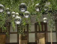 some shiny glass balls hanging from the side of a building with trees in front of it