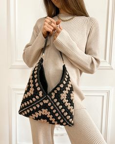 a woman is holding a black and white bag with flowers on the front, while standing in front of a door