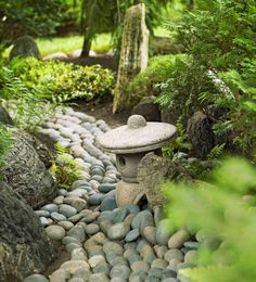 a stone lantern in the middle of a garden with rocks and trees around it, surrounded by greenery