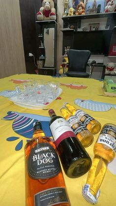 two bottles of wine are sitting on a yellow tablecloth with other items in the background