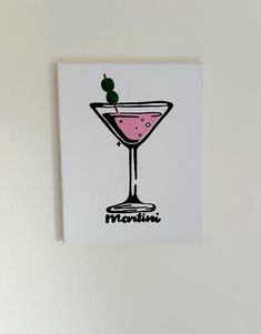 a card with a martini in it on a white wall next to a green plant