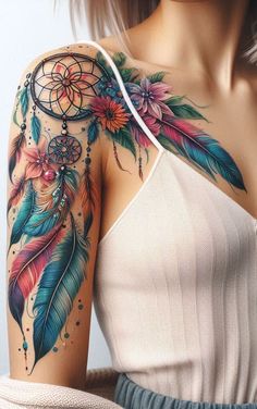 a woman's shoulder with colorful feathers and flowers on her arm, as well as a dream catcher tattoo