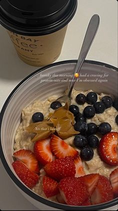 a bowl of oatmeal with strawberries and blueberries next to a cup of coffee