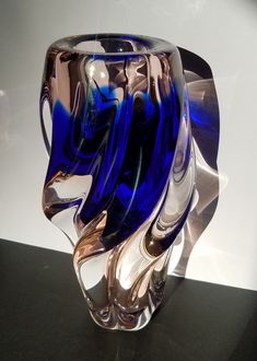 a blue glass vase sitting on top of a black table next to a white wall