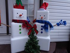 two snowmen standing next to each other in front of a house with a christmas tree