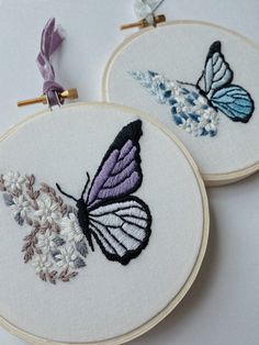 two embroidery hoops with butterfly designs on them, one is purple and the other is white