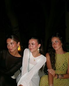 three beautiful women sitting next to each other in front of a dark room with lights