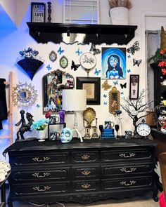 a black dresser topped with lots of assorted items next to a wall covered in pictures and clocks