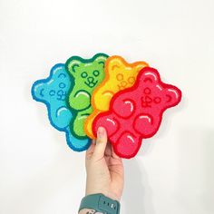 a hand holding four colorful teddy bears on a white wall with the number one in front of them