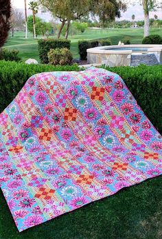 a quilted blanket sitting on top of a lush green field