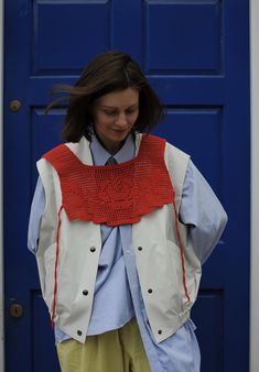 a woman standing in front of a blue door wearing a white vest and yellow pants