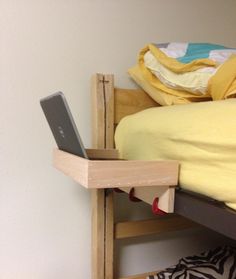 a laptop computer sitting on top of a wooden shelf next to a bed with yellow sheets