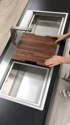 a person standing in front of a sink with a cutting board on top of it