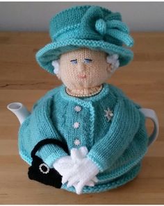 a knitted doll sitting on top of a wooden table next to a tea pot