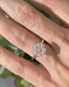 a woman's hand with a diamond ring on top of her finger and a plant in the background