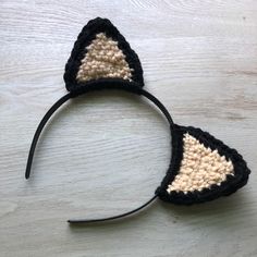 a crocheted black and white cat ears headband on top of a wooden table