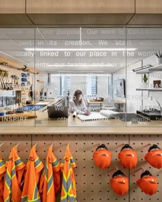 a woman working on her laptop in an industrial setting with orange safety vests hanging from the wall