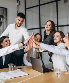 a group of business people giving high fives to each other in front of a laptop computer