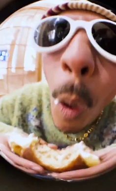 a man wearing sunglasses and holding food in front of his face while looking at the camera